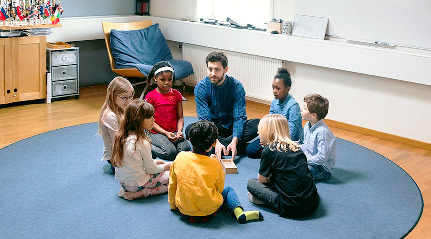 En grupp förskoleelever sitter på golvet med en lärare