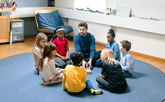 En grupp förskoleelever sitter på golvet med en lärare
