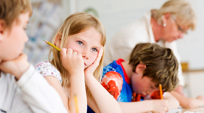 En elev som funderar på lektionen medan klasskamraterna blir hjälpa av läraren