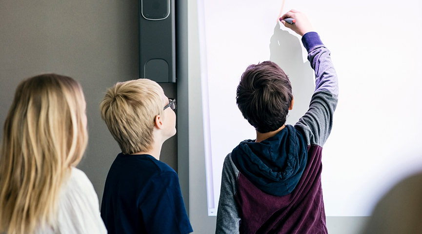 Tre elever håller en presentation och skriver på en whiteboard
