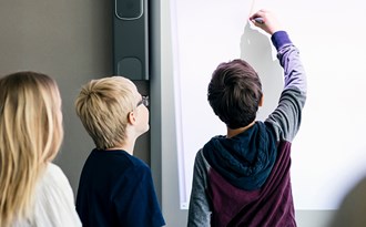 Tre elever håller en presentation och skriver på en whiteboard