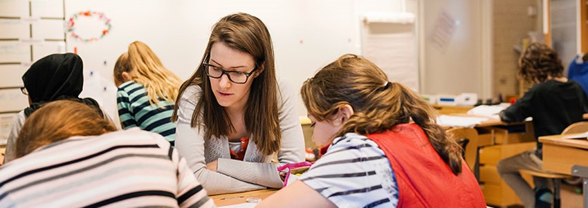 En lärare hjälper två mellanstadieelever i ett klassrum vid bänkarna