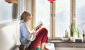 En högstadieelev läser en bok vid ett fönster