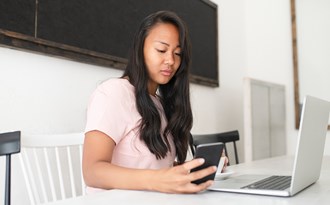 En gymnasieelev sitter vid sin dator och mobil och studerar