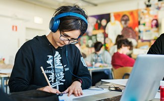 En gymnasieelev med hörlurar sitter och studerar under en lektion vid en dator 