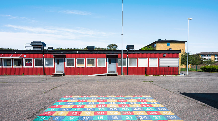 Skolbyggnad och skolgård under klarblå himmel